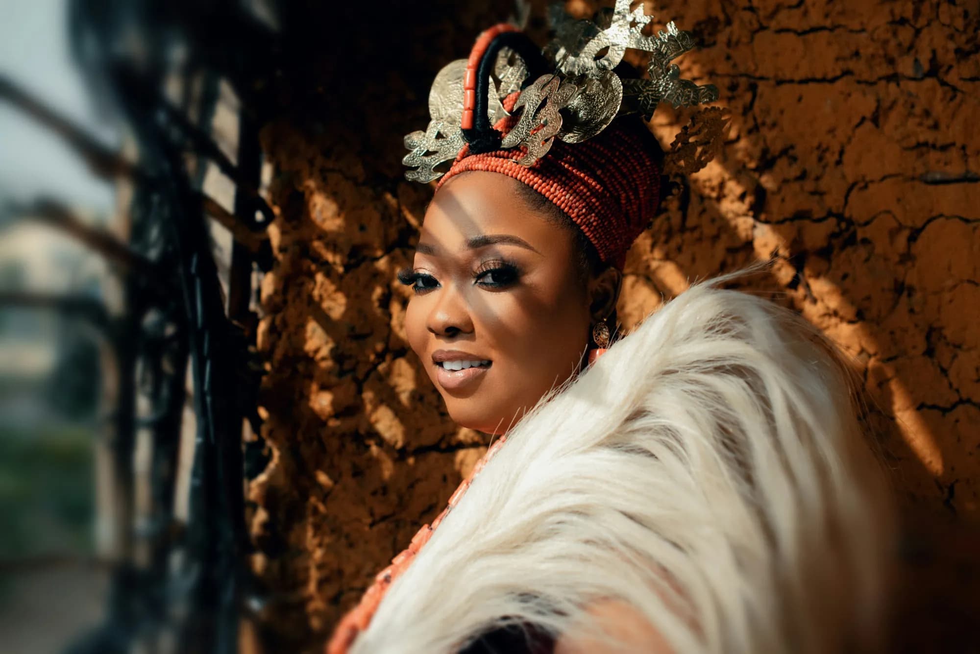A bride in a coral-beaded headdress and ivory feathers, smiling over her shoulder in warm light